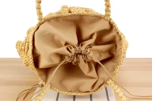 Top view detail of woven straw bucket bag with drawstring inner lining on wooden surface.