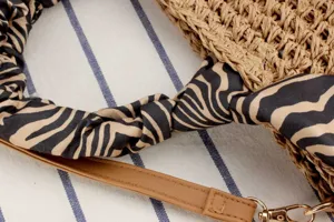 Close-up of handmade straw woven bag detail with zebra print scarf handle and leather strap.