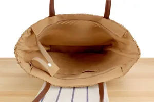 Interior detail view of a large capacity straw tote bag with brown leather handles and beige lining.