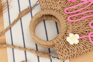 Detailed view of handmade woven straw crossbody bag with round handle and pink string decor.