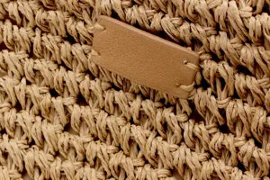 Close-up detail view of the handmade woven straw bag featuring a blank leather tag.