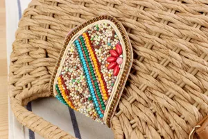 Nahaufnahme einer handgeflochtenen Strohtaschenklappe mit bunten Perlen und Kettenrand.