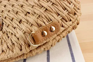Detailansicht der handgeflochtenen Strohtasche mit PU-Lederriemen und goldenen Metall-Beschlägen.