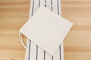 Close-up detail shot of a plain beige cotton drawstring pouch resting on striped fabric.