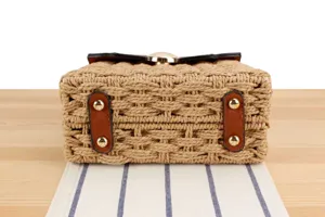 Nahaufnahme des Stroh-Handtaschendetails, Textur, braune Lederlasche und Metallnieten.