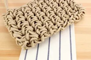 Close-up detail of handmade woven rope shoulder bag on striped fabric, stylish and textured.