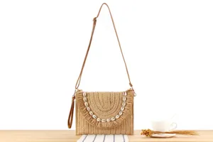 Close-up detail view of the woven straw crossbody bag featuring seashell fringe and slim strap.