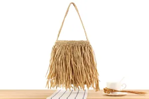 Gros plan d'un sac à main en paille élégant avec des détails de franges sur table.
