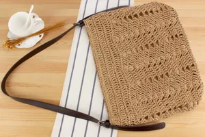 Vue détaillée du sac bandoulière tissé en paille avec motif ajouré et lanière marron.