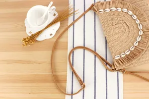 Detail shot of a woven straw crossbody bag featuring seashell and fringe decorations.