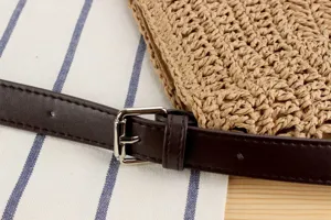 Gros plan detail de sac en paille tressee main avec laniere en cuir marron et boucle metal.