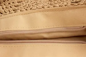 Vue rapprochée du sac en paille tressée montrant la fermeture éclair et la doublure solide.