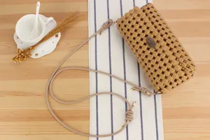Detail shot of a woven shoulder bag in camel color with metal plate, styled on table.