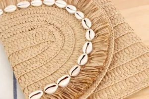 Close-up view of a boho straw woven clutch bag decorated with natural cowrie shells and fringe.