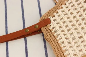 Close-up detail of handmade woven crochet shoulder bag with brown leather strap and metal rivets.