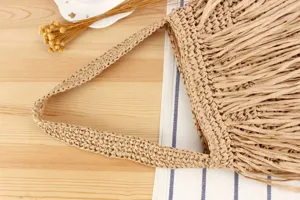 Gros-plan sur la poignée et les franges du sac fourre-tout en paille, style casual.