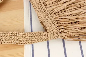 Gros plan sur la texture du sac à main en paille, montrant un savoir-faire et franges.