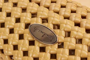 Detailed close-up of a yellow woven bag featuring an elegant handmade metal tag plaque.