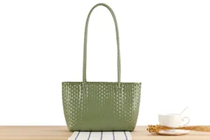 Green woven plastic tote bag displayed on wooden table with elegant floral props detail.