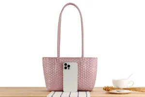 Pink plastic woven tote bag close-up, casual beach vacation picnic handbag display.
