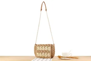 Detail shot of a handmade woven straw crossbody bag with chain strap and metal lock closure.