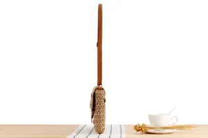 Detailed side view of a vintage woven straw crossbody bag with brown leather strap on wooden table.