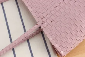 Close-up detail of pink woven plastic basket bag texture, handmade style and braided handle.