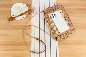 Detailed straw woven crossbody bag styled with chain strap on wooden background