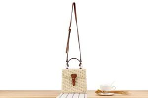 Detailed view of the handmade woven straw crossbody bag with leather strap and front buckle.