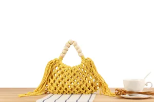 Detail view of a yellow handmade macrame woven handbag with wooden bead handles and cute fringe.
