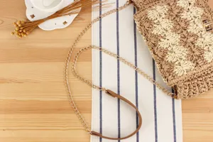 Detail view of the hand-woven straw crossbody bag with metallic chain strap and lock.