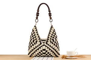 Detail view of black and white crochet shoulder bag with wooden bead handle on wooden table