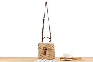 Detail view of handmade woven straw crossbody bag with brown leather strap and buckle clasp.
