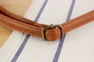 Detailed view of brown faux leather bag strap with antique brass adjuster buckle, close up.