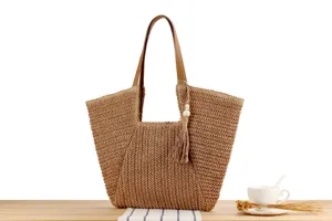 Close-up detail of the straw woven tote bag featuring a brown leather handle and tassel.