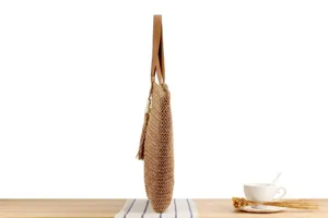 Side detail view of a stylish woven straw shoulder bag with leather handles and chic tassel decor.