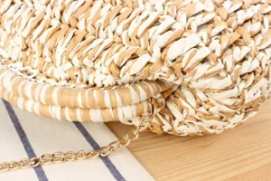 Close-up detail shot of handmade two-tone woven straw shoulder bag with elegant metal chain.