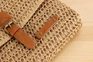 Detailed close-up of straw woven bag showcasing texture, PU leather strap and metal hardware.