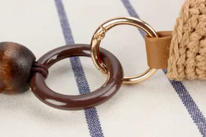 Primo piano dei dettagli della borsa in paglia con accessori metallici e perla in legno.