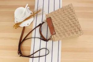 Handmade woven straw crossbody bag detail, featuring brown PU leather strap and structured body.