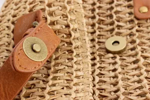 Close up view of woven straw bag texture with brown leather strap and metal magnetic snap.