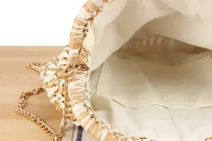 Close-up detail view of handmade woven straw bag interior lining and gold chain strap.