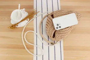 Handmade beige crochet crossbody bag detail with elegant pearl strap and phone display scene.