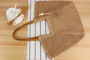 Casual straw woven tote bag with leather handles and tassel pendant for summer beach vacation.