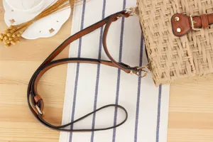 Detail view of the handmade woven straw crossbody bag with brown leather strap and metal buckle.