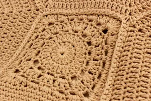 Dettaglio di una borsa a tracolla intrecciata a mano che mostra una complessa trama all'uncinetto.