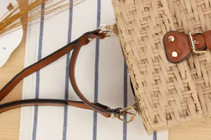Close-up detail of handmade woven straw handbag with brown PU leather straps and gold hardware.