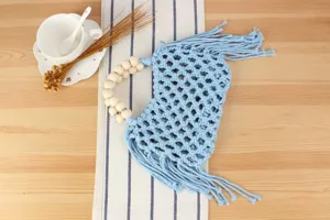 Detailed view of the light blue macrame woven handbag featuring a wooden bead handle and fringes.