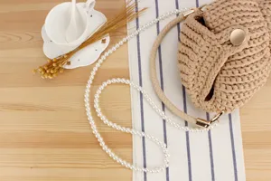 Detail shot of handmade woven crossbody bag with pearl chain and beige braided handle.