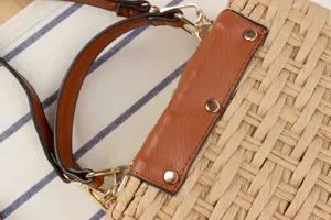 Handmade straw woven handbag with brown leather handle and metal rivets for daily bags.